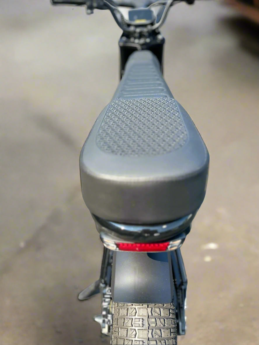 Close-up of a motorcycle seat with a textured surface on a gray pavement background